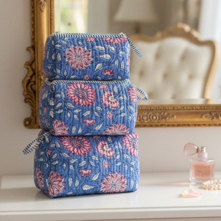 Set of three blue floral-patterned makeup bags on a dresser with a mirror in the background.