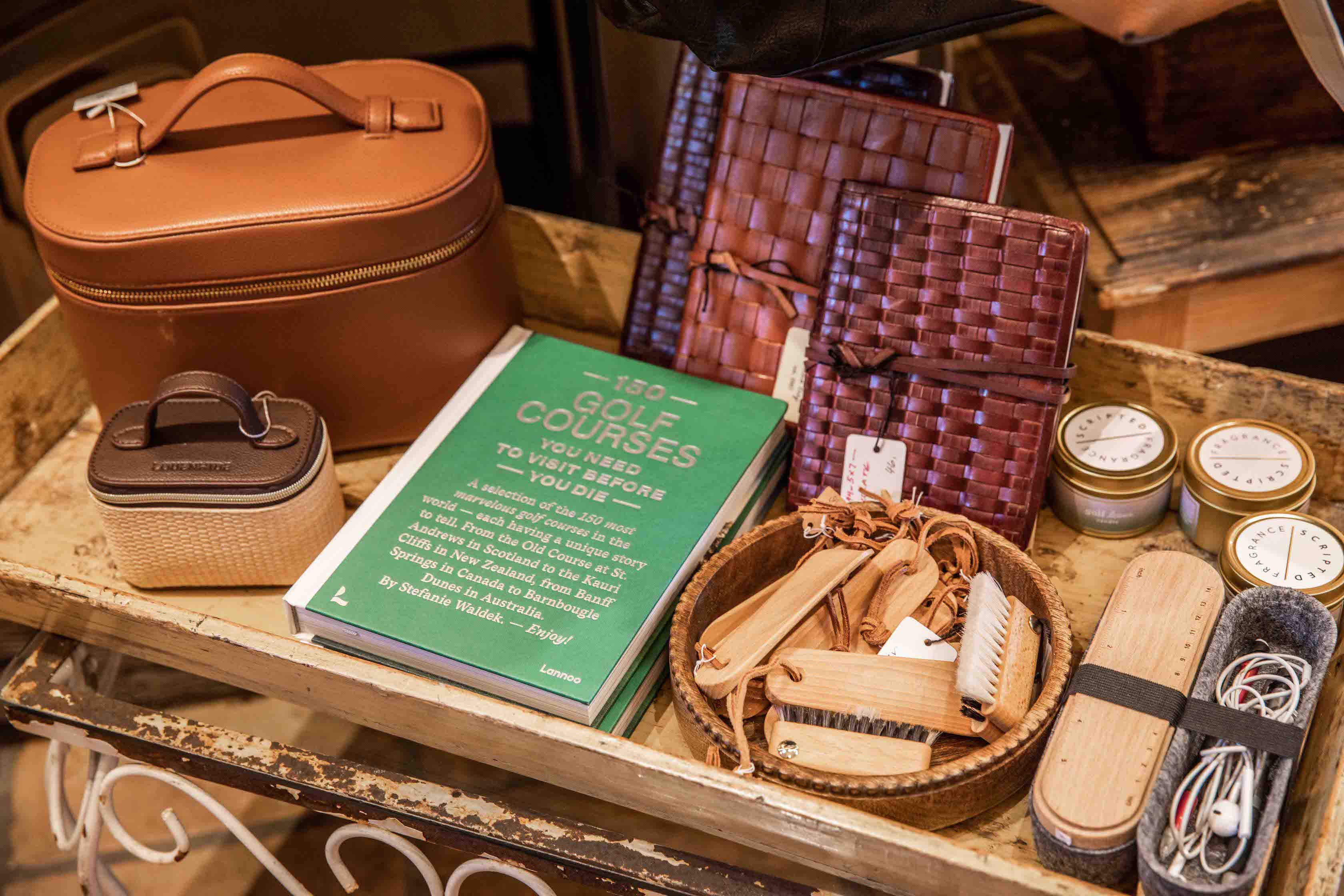 Collection of gift items including a brown leather box, green book, and wicker basket on a wooden tray.