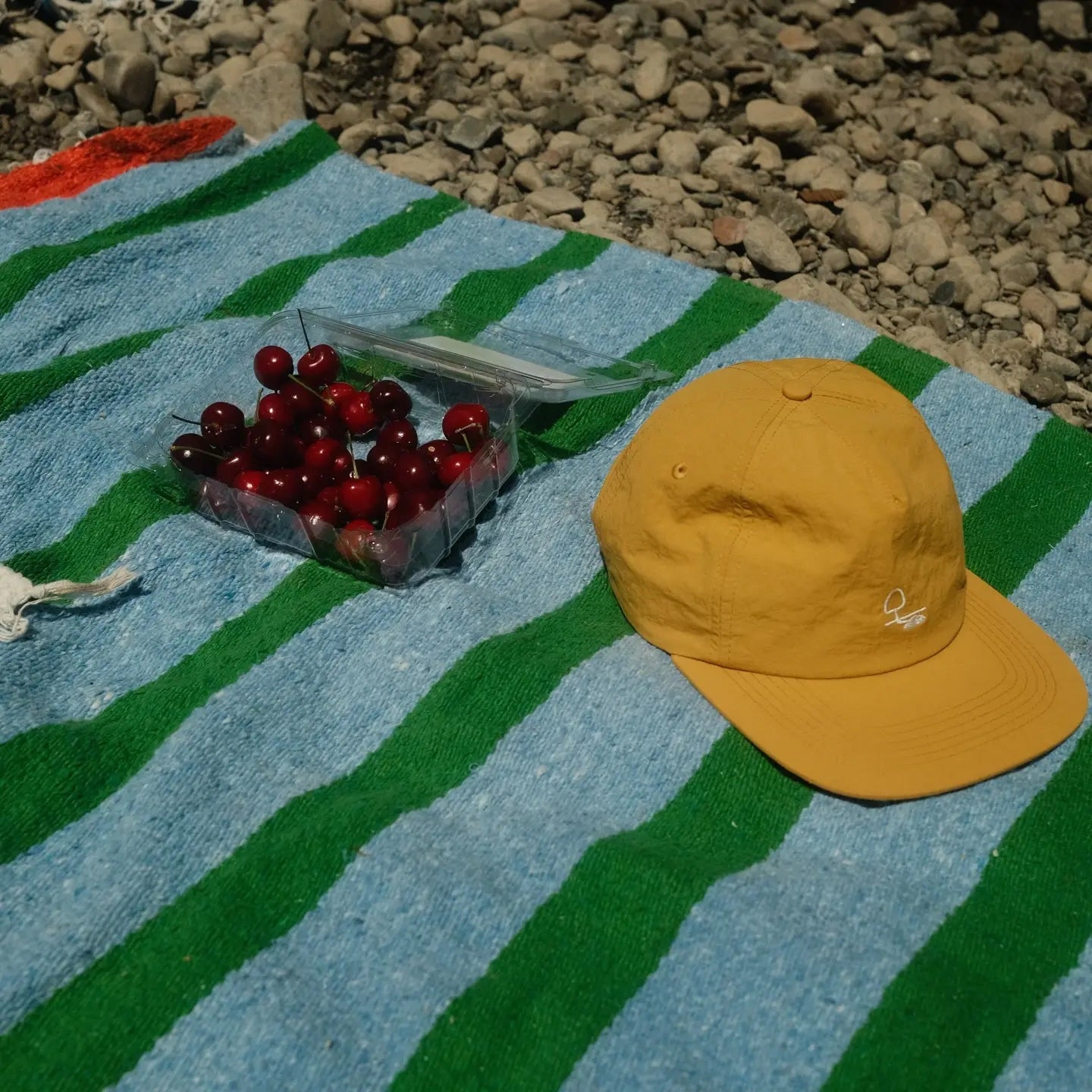 Yellow cap on a blue and green striped towel with cherries and a transparent container.