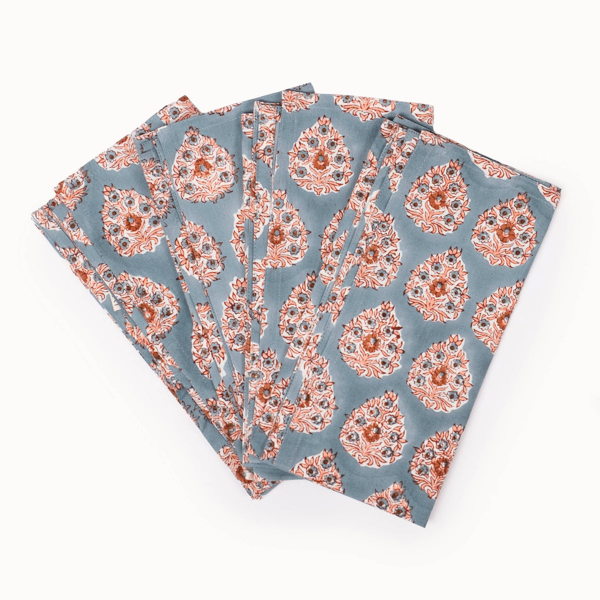 A set of four folded square fabric napkins, featuring a dusty slate blue background with a repeating orange and white floral medallion pattern, arranged in a fan shape on a plain white background.