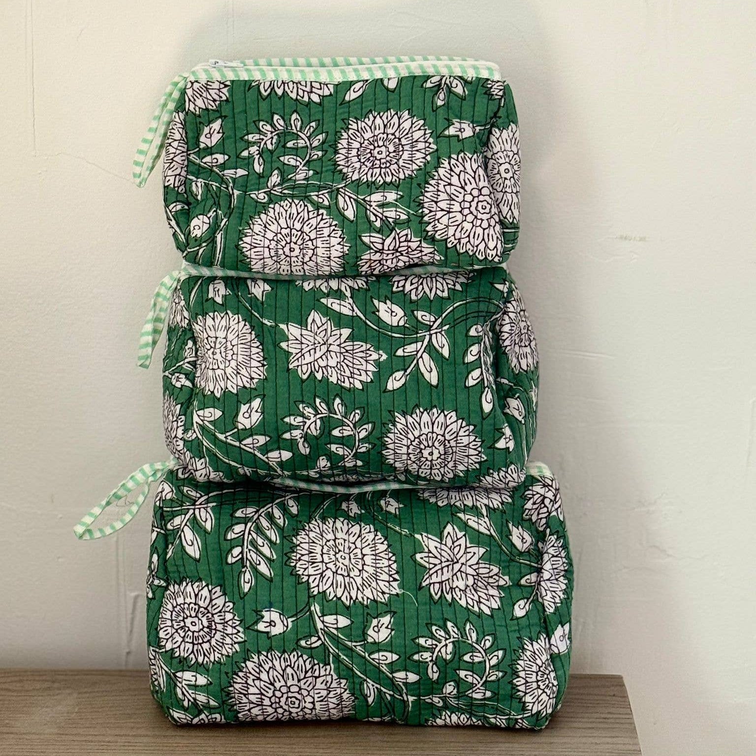 Stack of green floral-patterned bags on a wooden surface with a white background