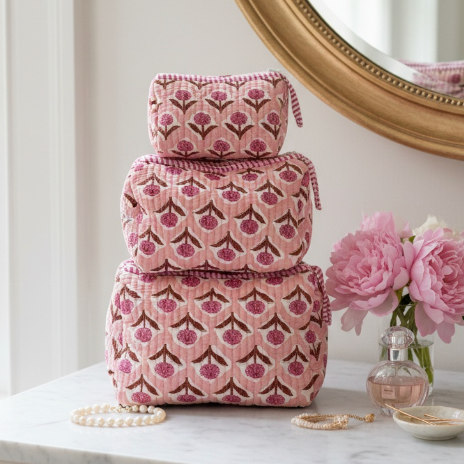 Stack of pink patterned boxes on a marble surface with a mirror and flowers in the background