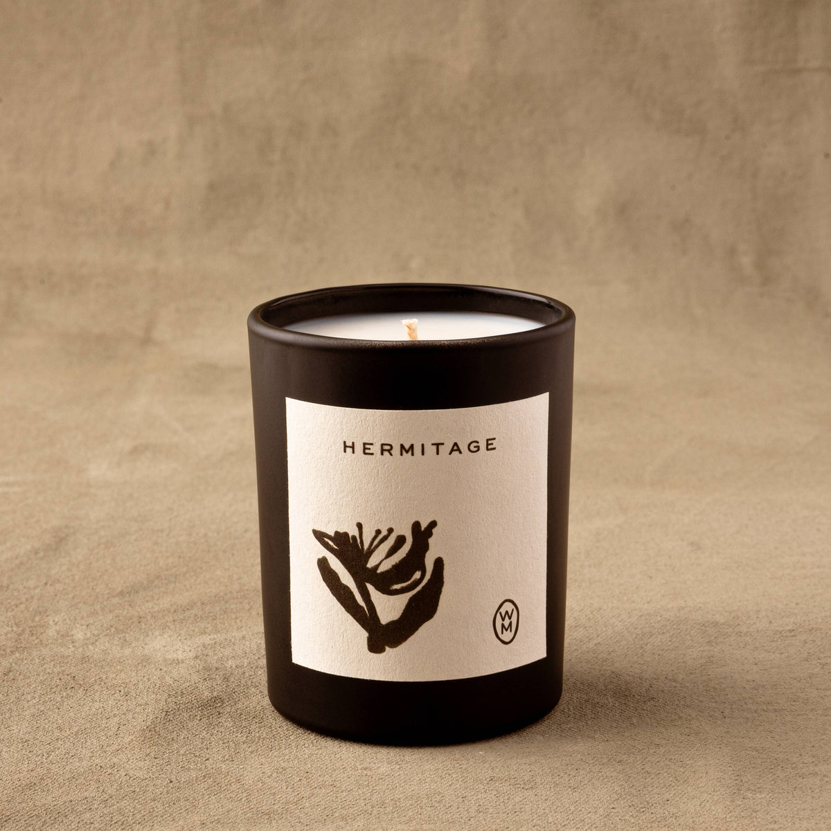 Candle in a black container with 'Hermitage' label on a beige background