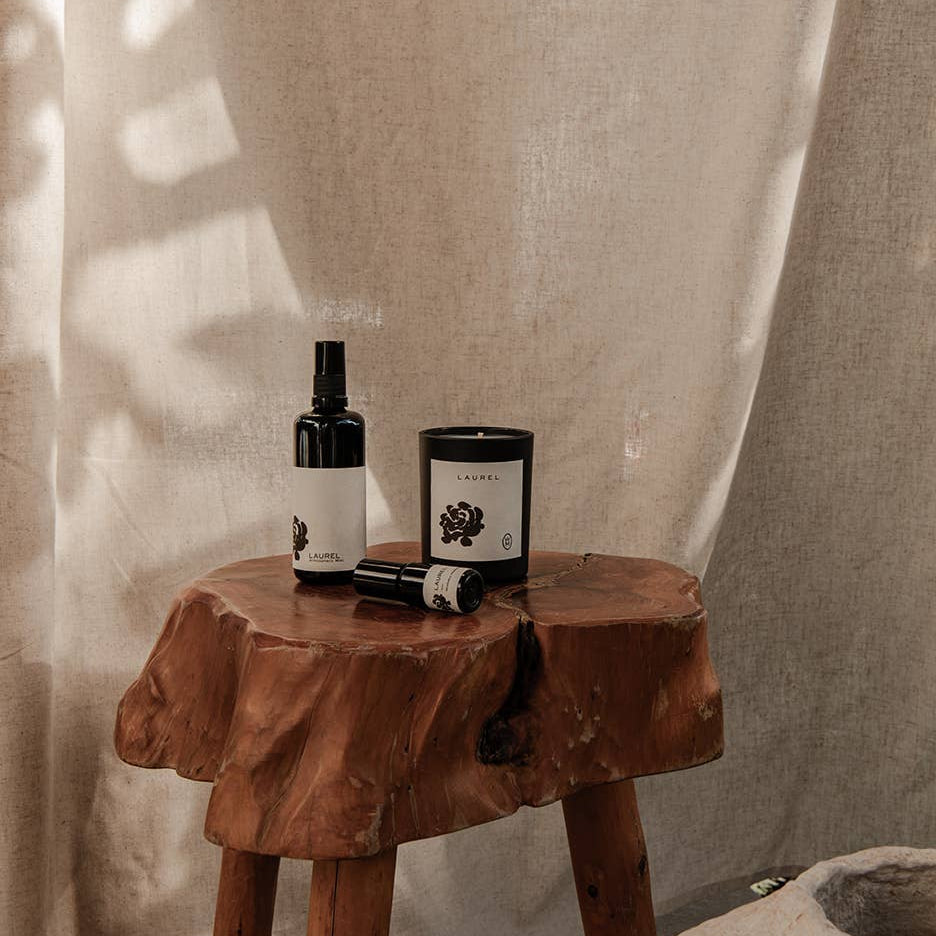 Wooden stool with a bottle and a candle against a beige curtain