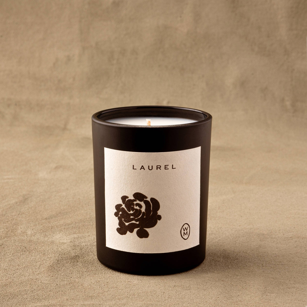 Candle in a black container with a white label featuring a black rose design on a beige background