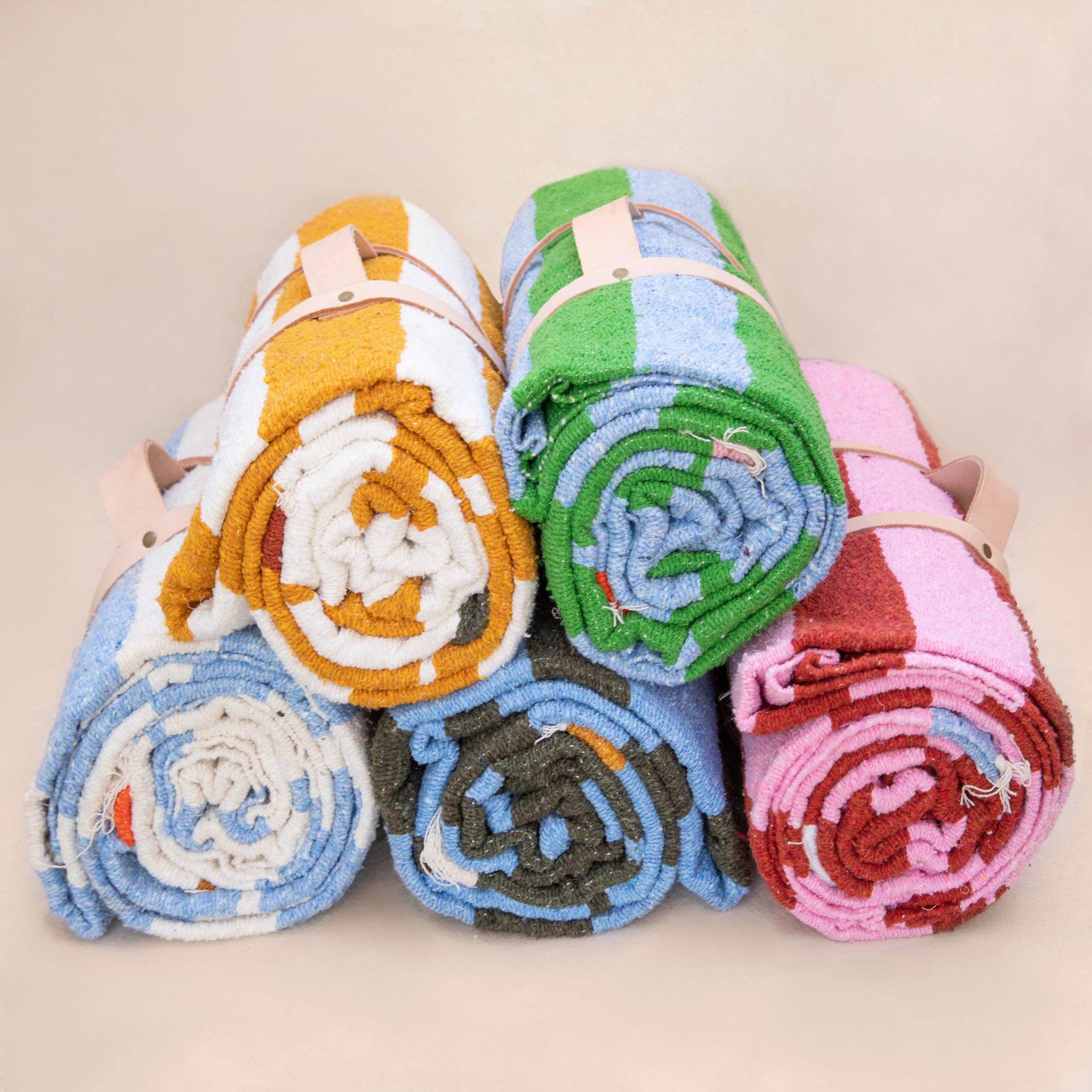 five colors of striped beach blankets rolled up in a stack
