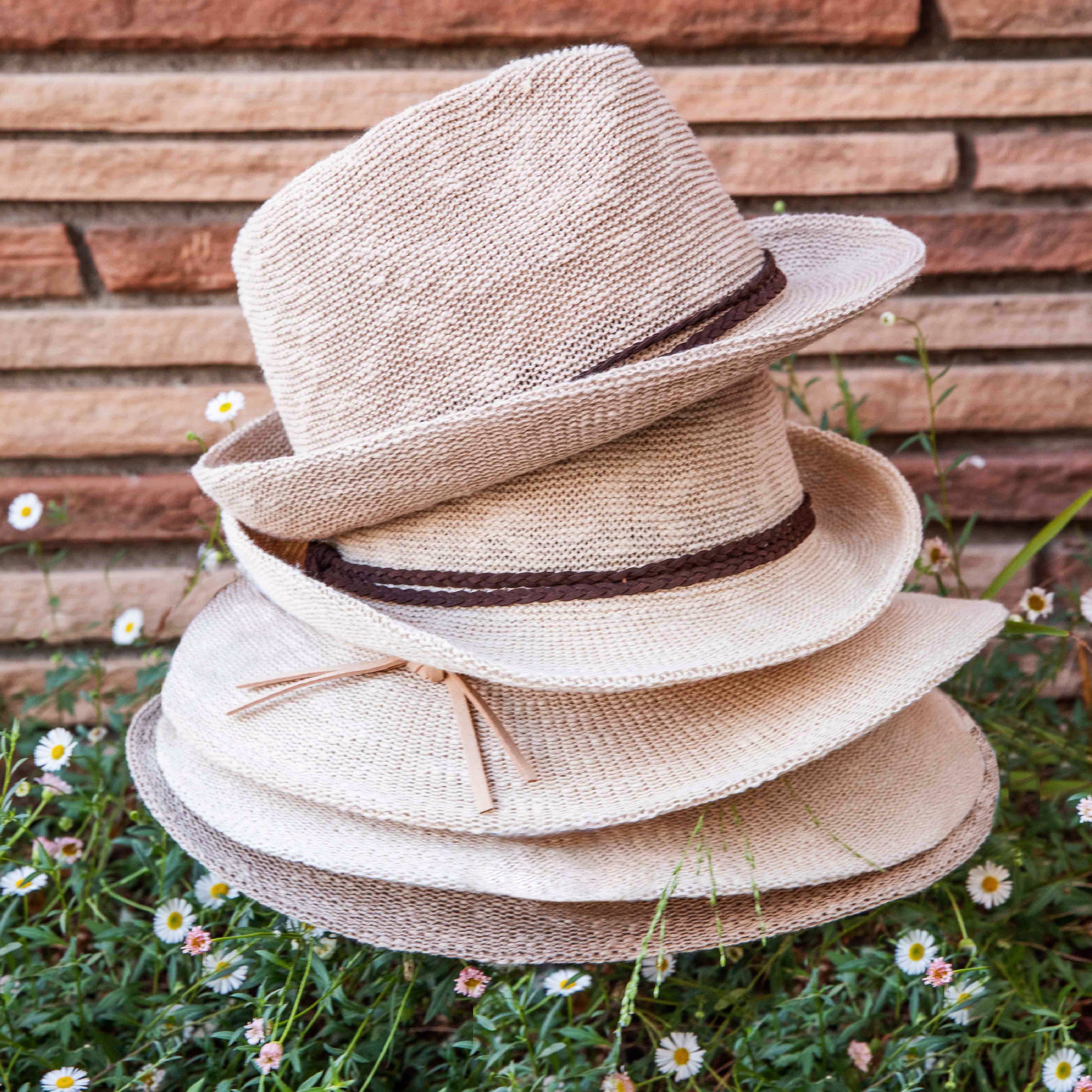 Stack of straw hats with a brown ribbon against a wooden wall and grass background