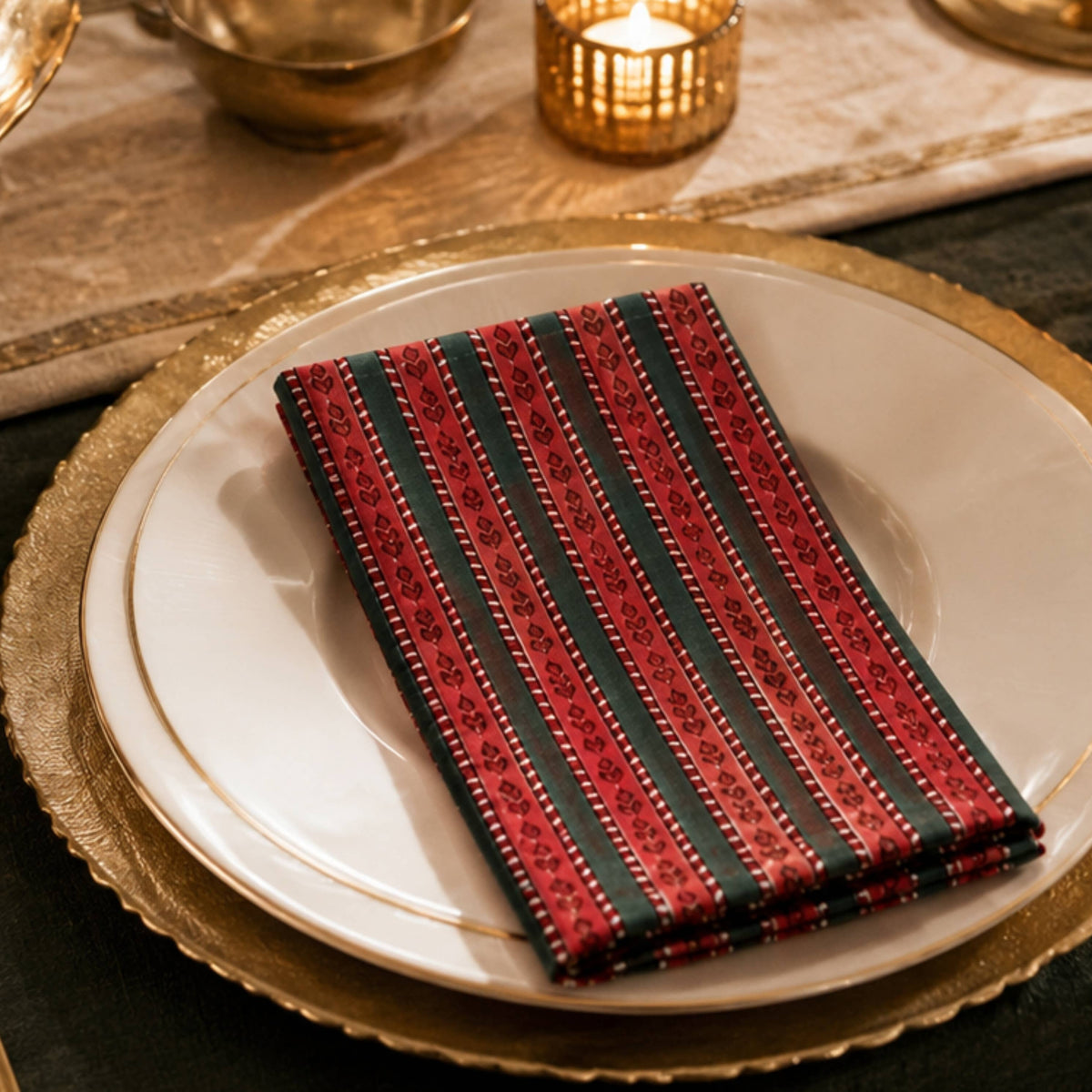 A folded red and black striped patterned napkin with gold detailing, styled on a white plate with a gold charger plate at a formal table setting.