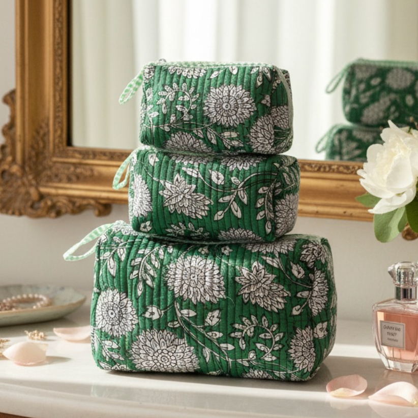 Set of green floral-patterned makeup bags on a vanity with a mirror and flowers.