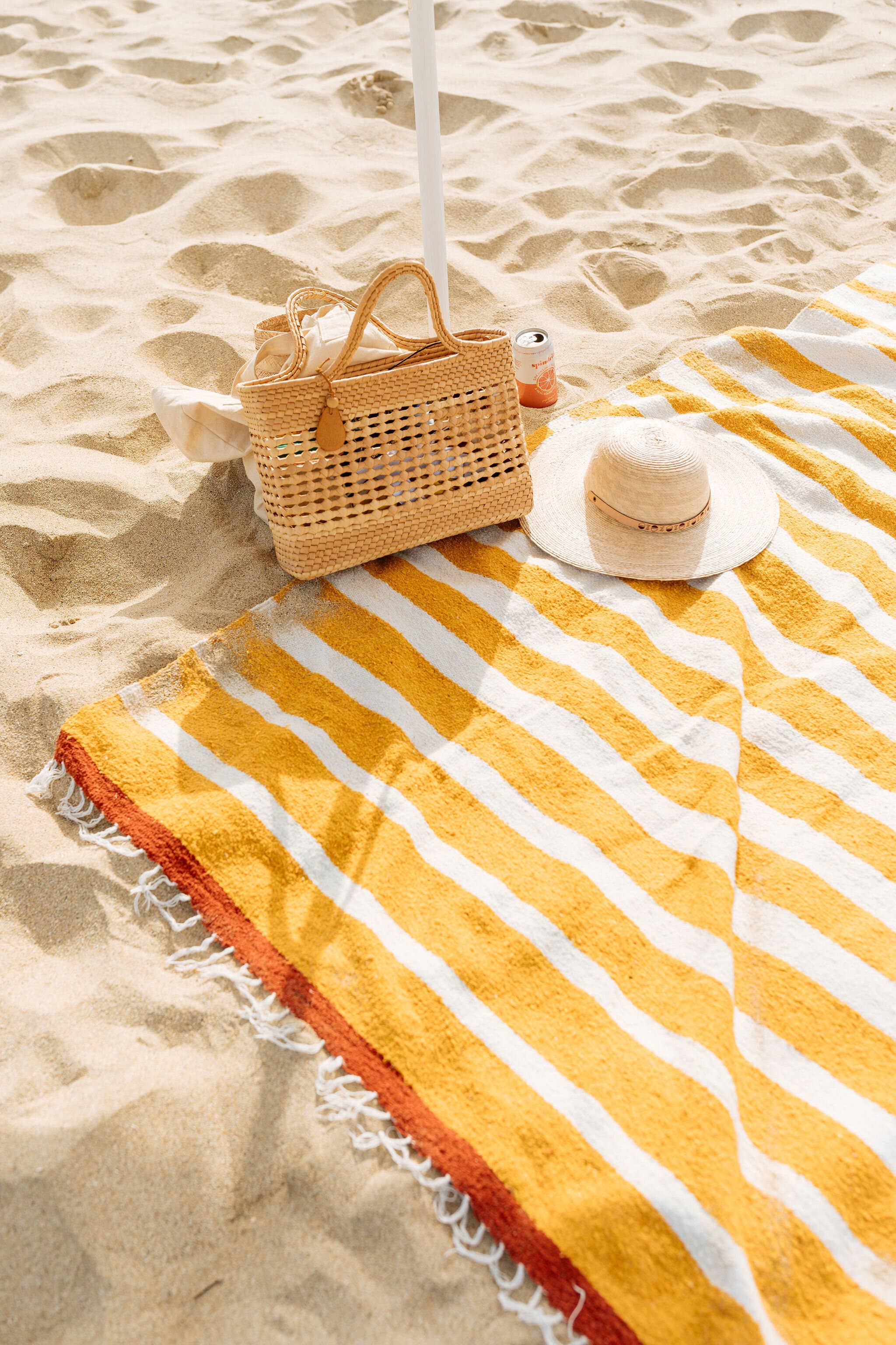 Yellow striped towel on a sandy beach with a woven bag and sun hat.