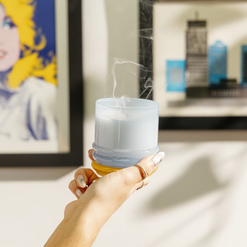 Hand holding blue glass jar candle that has just been blown out